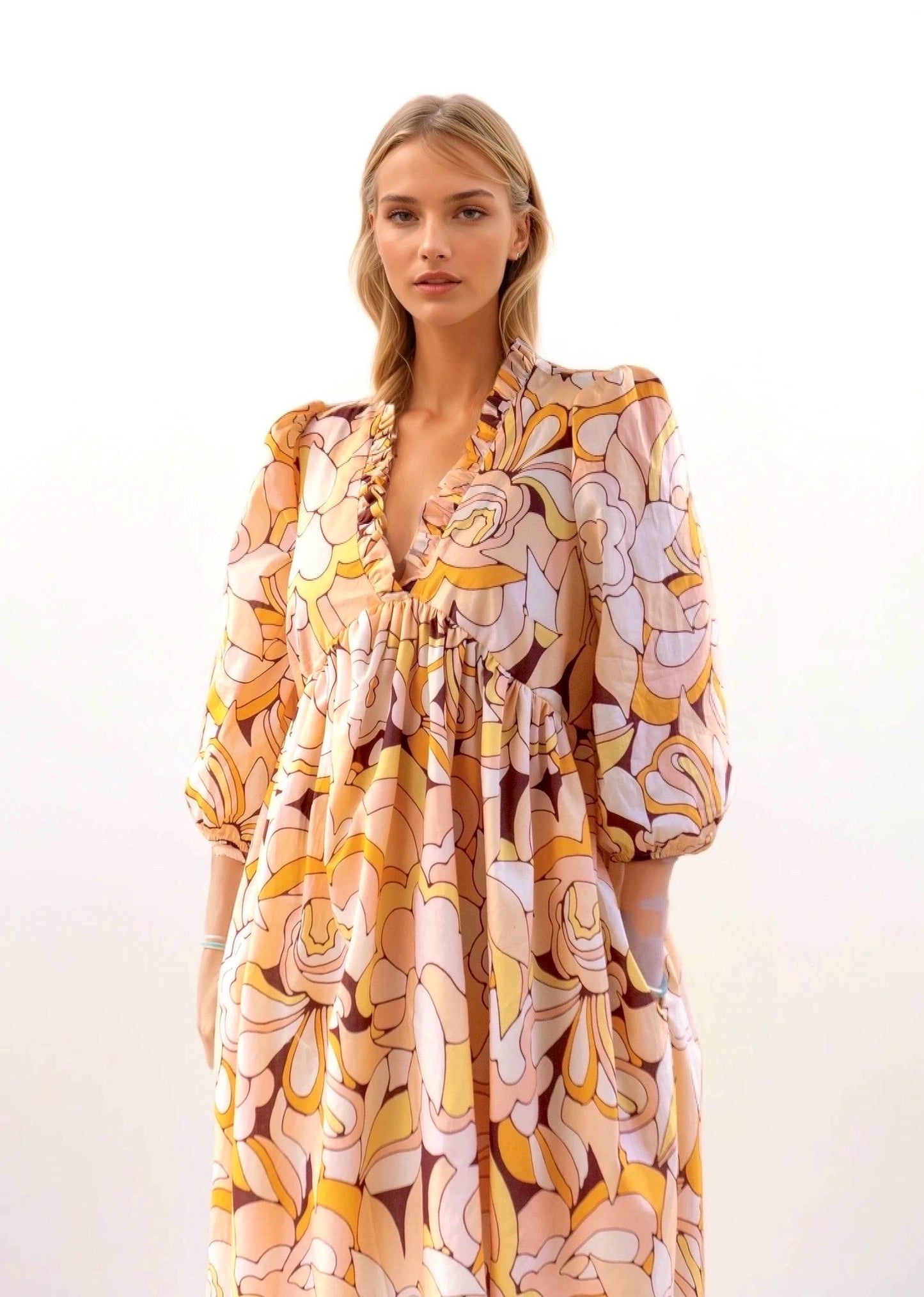 May include: A long, flowing dress with a vibrant floral pattern in shades of peach, yellow, and brown. The dress features a V-neckline with ruffle detailing, three-quarter sleeves, and a gathered waist. The fabric has a silky appearance.