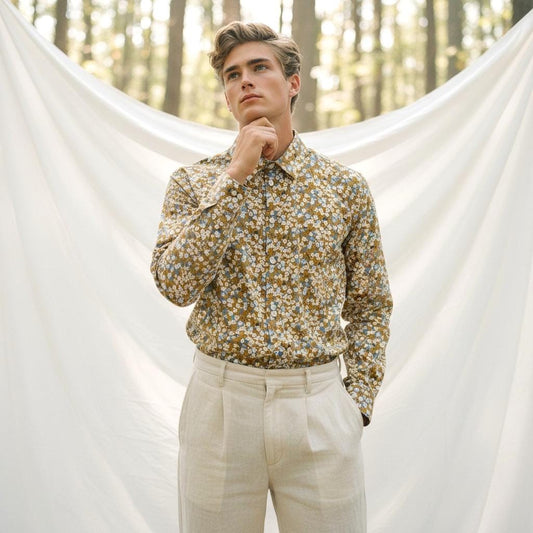 May include: A long-sleeved button-down shirt with a floral pattern in shades of yellow, blue, and white. The shirt is paired with light beige pleated trousers. The background features a white curtain and a forest.